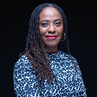 Headshot of a smiling woman in a blue & white top against a black background.