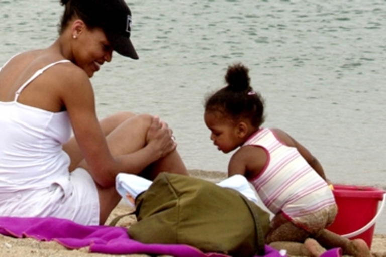 Mother and toddler play on a sandy beach by the water's edge.