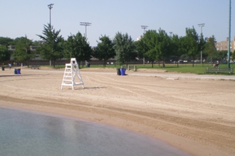 Empty sandy beach with lifeguard chair. Adjacent grassy area with park benches.