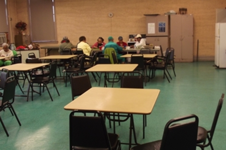 People sit at tables in a large room with teal flooring.