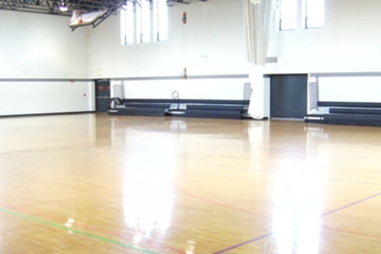 Empty gymnasium with polished wooden floor and retracted bleachers.