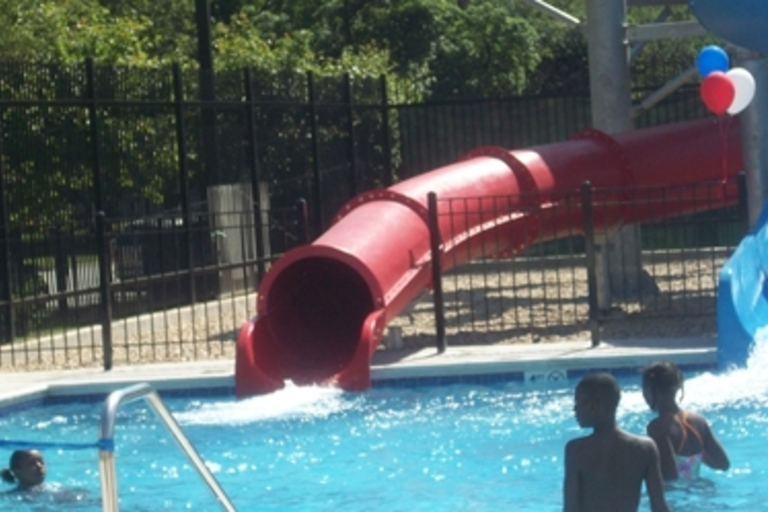 Red waterslide emptying into a swimming pool with children playing.
