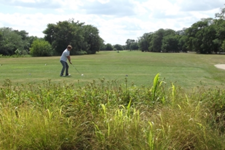 Golfer tees off on a sunny day. Another person watches from a golf cart.