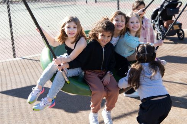 Five children enjoy a saucer swing at a playground.