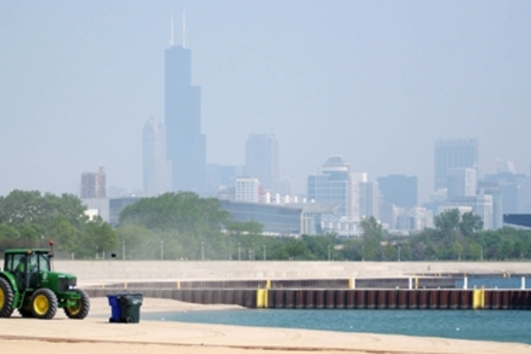 Tractor cleaning a beach with Chicago skyline in background.