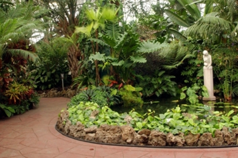 Lush indoor botanical garden with a statue and pond.
