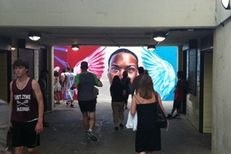 Mural of a face with wings in an underpass. People walk toward it.