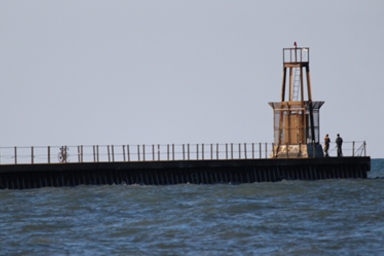 Small lighthouse at the end of a pier. People fish and bike nearby.