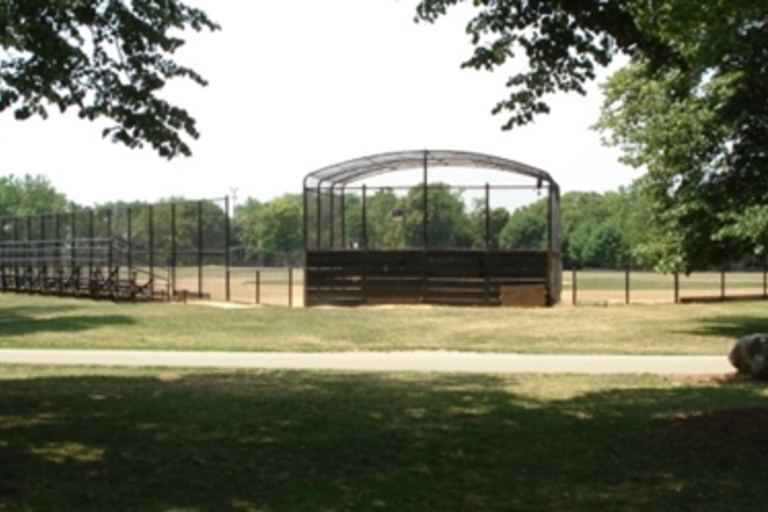 Empty baseball field with bleachers and batting cage.