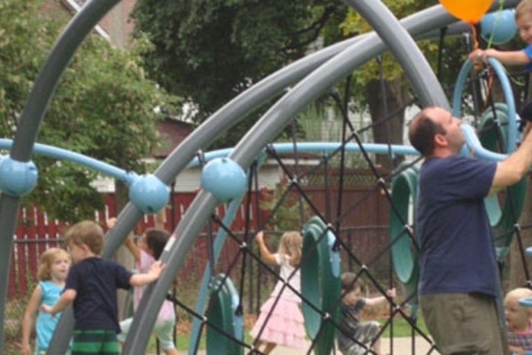Children and an adult play on a playground climber.