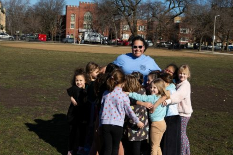 Group of children and their teacher huddle together in a park.
