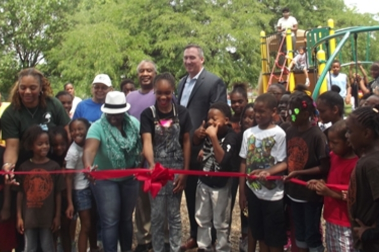 Group cuts a red ribbon at a park playground opening.
