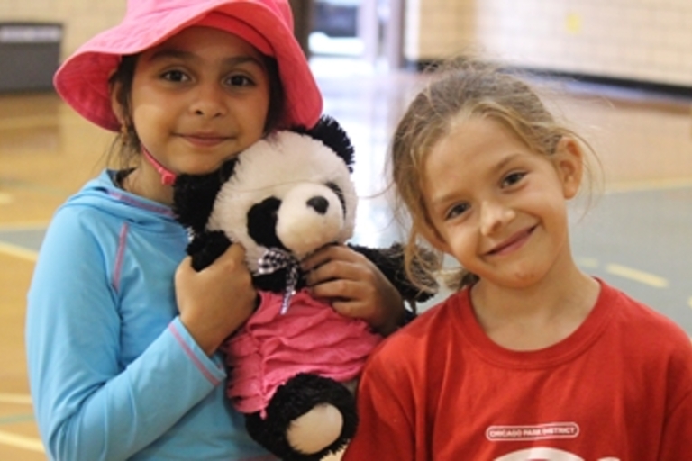 Two young girls smile, one holding a panda plush toy.
