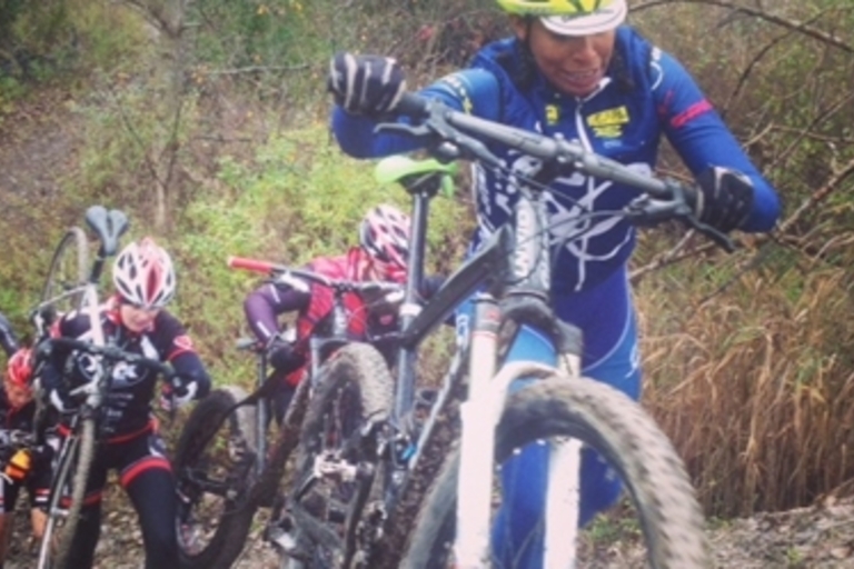 Cyclists carry their bikes uphill on a muddy trail.

