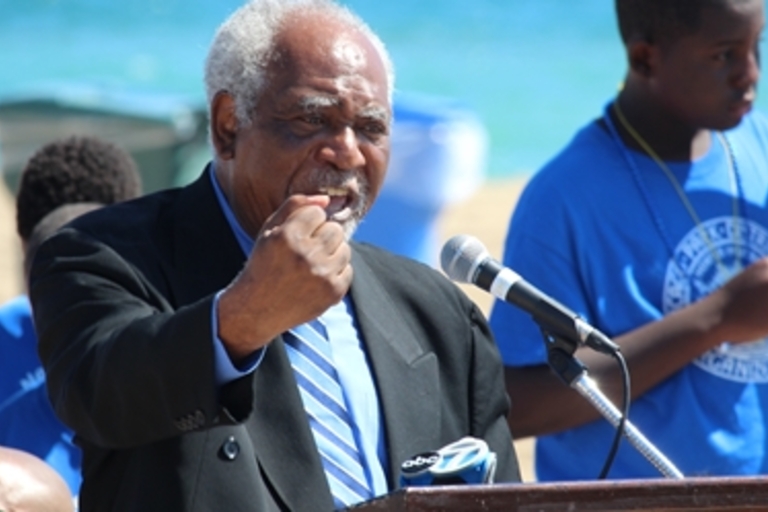 Man speaks at podium on beach.