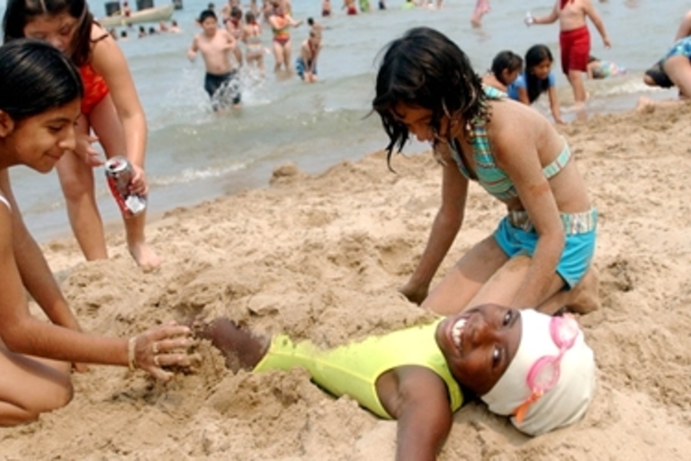 Children burying friend in sand at beach.
