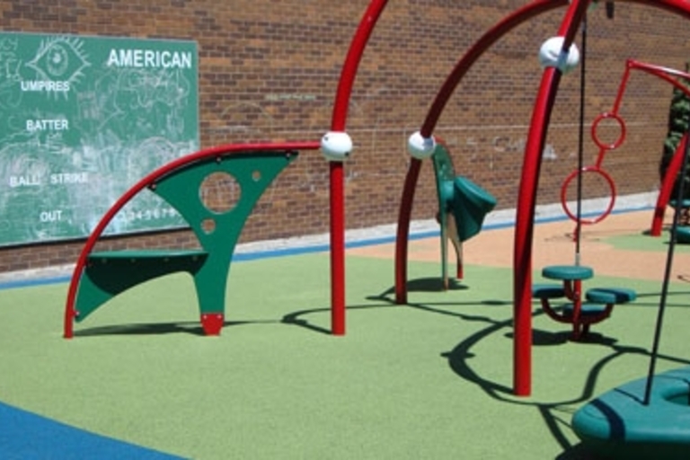Red and green playground equipment on a green and blue surface. Chalkboard in background.
