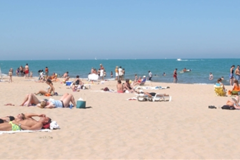 Crowded sandy beach on a sunny day. People sunbathe and swim. Lifeguard stand in background.
