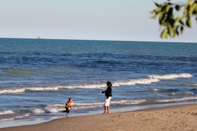 Child running from waves toward adult on beach.