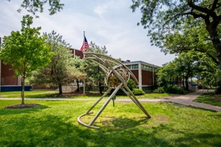 Abstract metal sculpture on a grassy lawn in front of a brick building with an American flag.