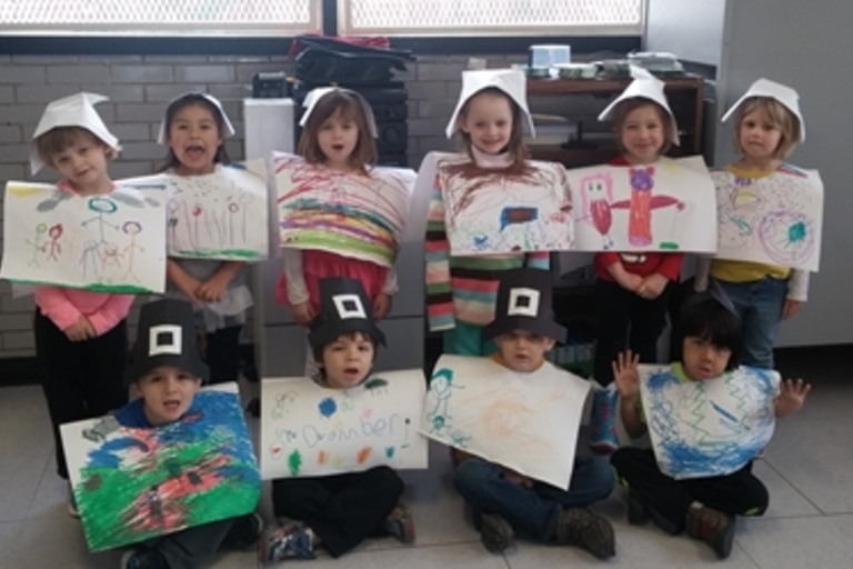 Children in pilgrim costumes display their Thanksgiving artwork.
