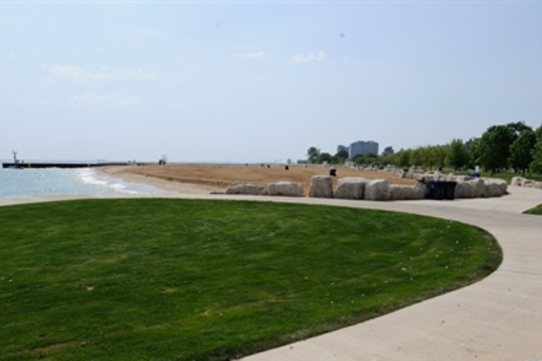Green lawn, sandy beach, and breakwater at a lakeshore park.