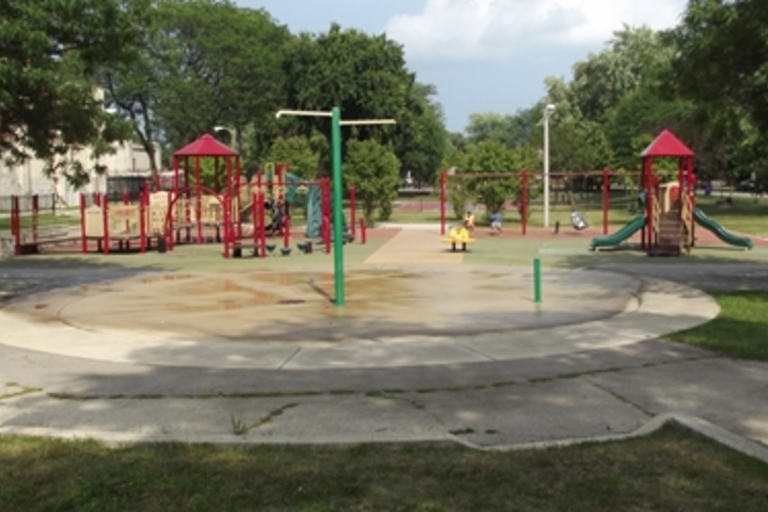 Empty playground with splash pad and a child with a backpack walking away.