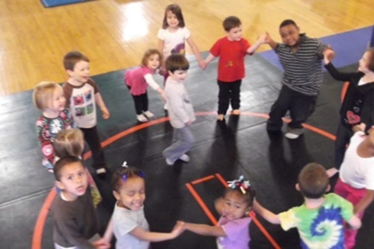 Children holding hands in a circle on a gym mat.