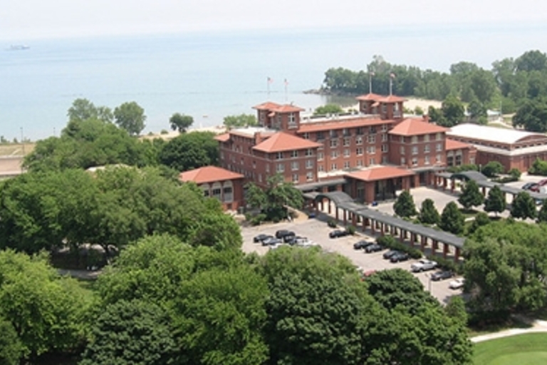 Aerial view of a large brick building near a lake, surrounded by trees and a parking lot.