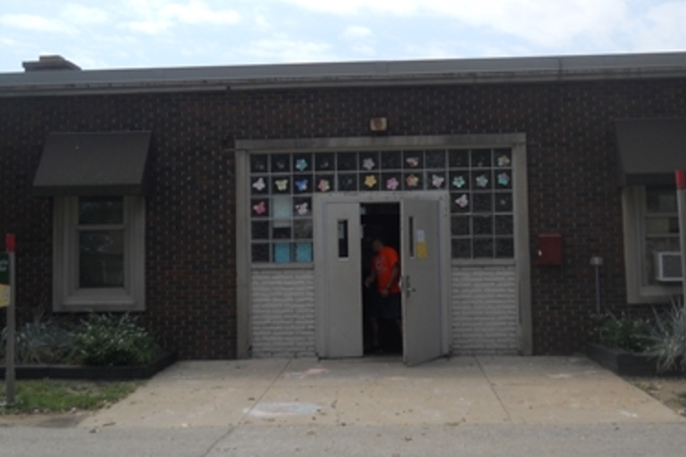 Brick building with open double doors and colorful artwork in the window above.