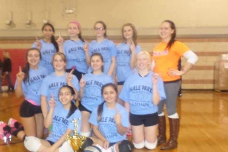 Girls volleyball team poses with trophy in gym.