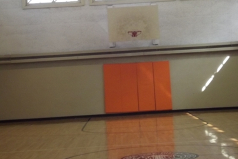 Empty indoor basketball court with orange padding on the wall.