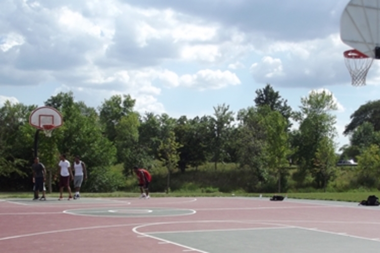 Outdoor basketball court with several players on a sunny day.
