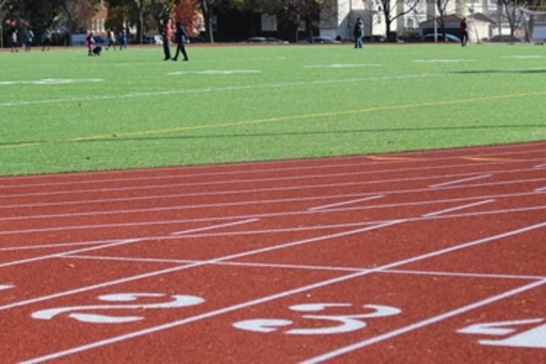 Red running track with white lane numbers and green playing field in background.
