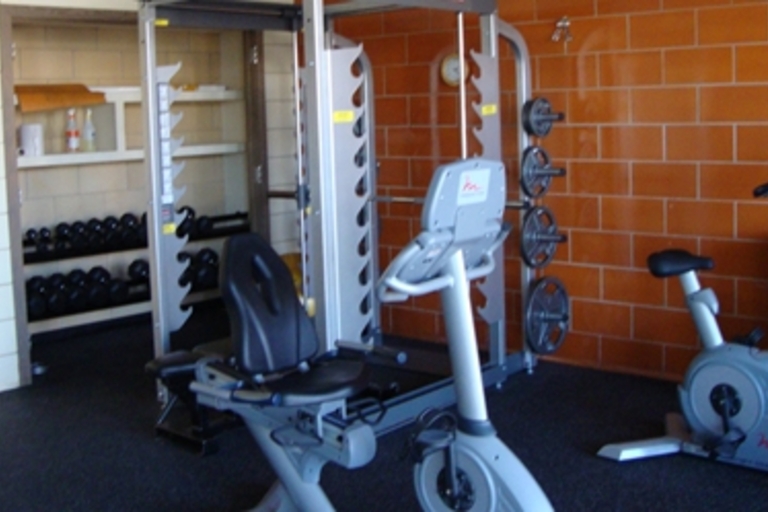 Small fitness room with weight machine, recumbent bike, upright bike, and free weights.
