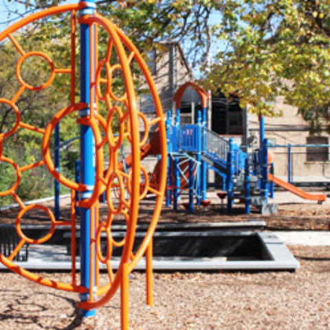 Orange and blue playground climbing structure.  A larger playset is visible in the background.