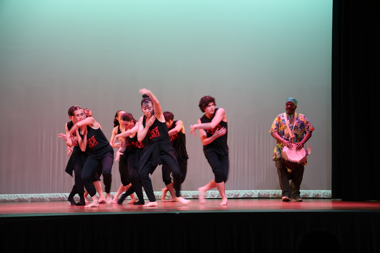 Dancers in black with a drummer on a stage.