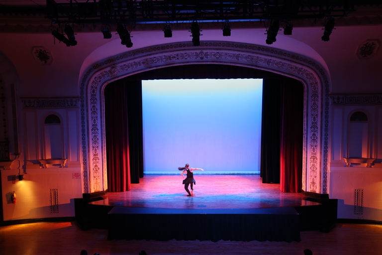 Dancer performs on stage, bathed in blue and pink light.