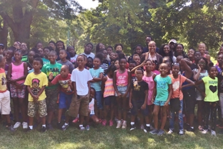 Large group of children and adults pose for a photo in a park.
