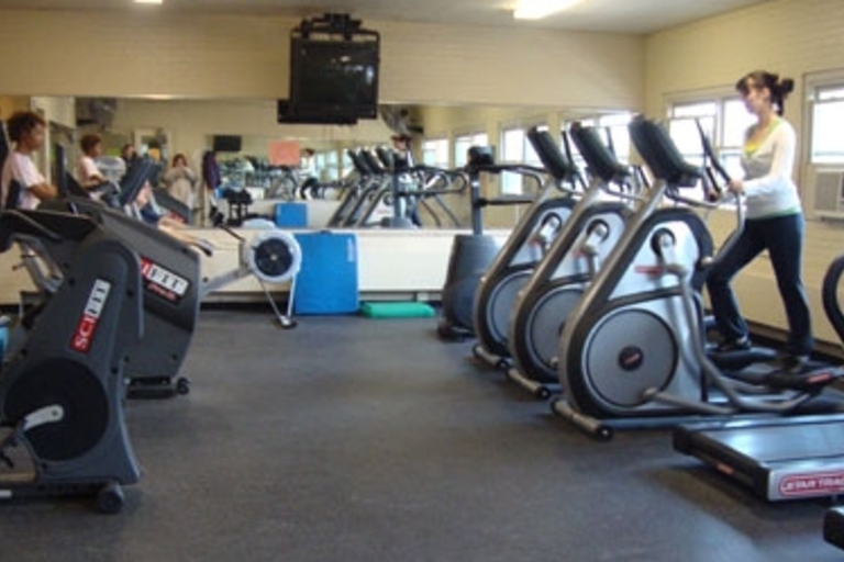 College gym with cardio equipment and a woman using an elliptical.
