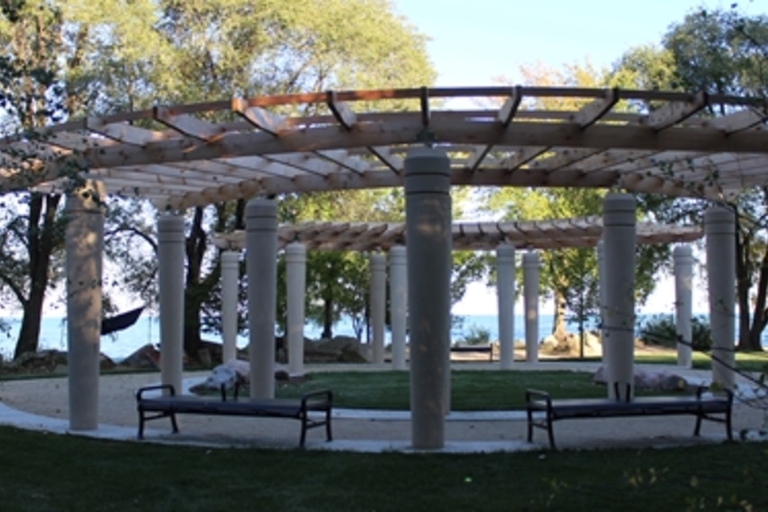 Circular pergola with benches in a park setting overlooking water.