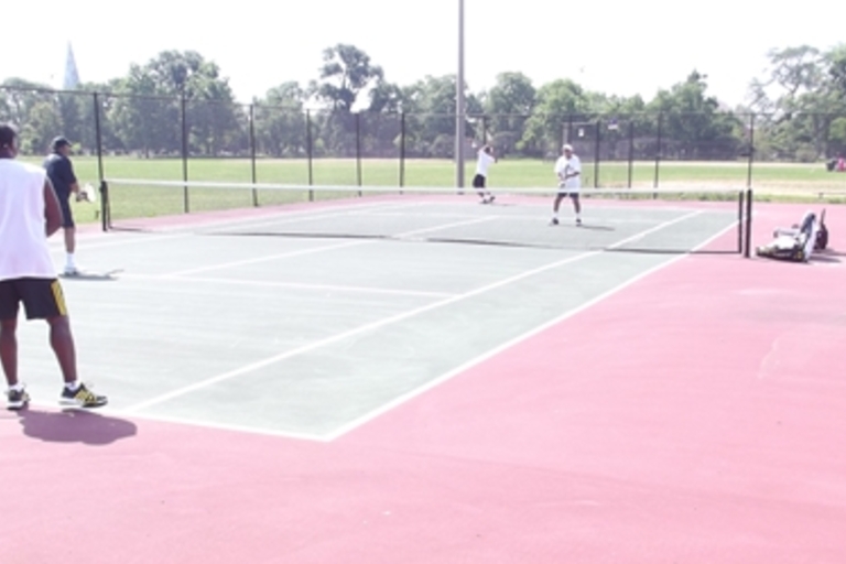 A doubles tennis match on a red and green court.