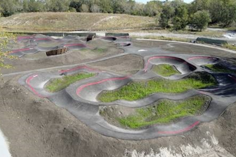 Pump track with paved trails and grassy mounds.