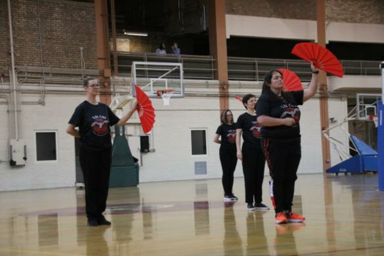 Four women practicing Tai Chi fan form in a gymnasium.