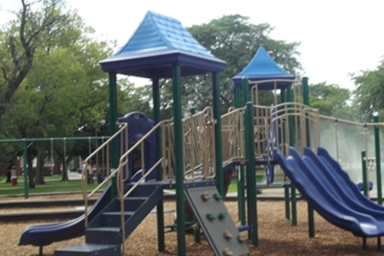 Playground with blue slides and climbing structures. Swings in the background.
