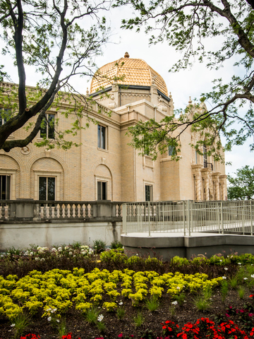 Beige brick building with gold dome, ramp, and flowerbeds.