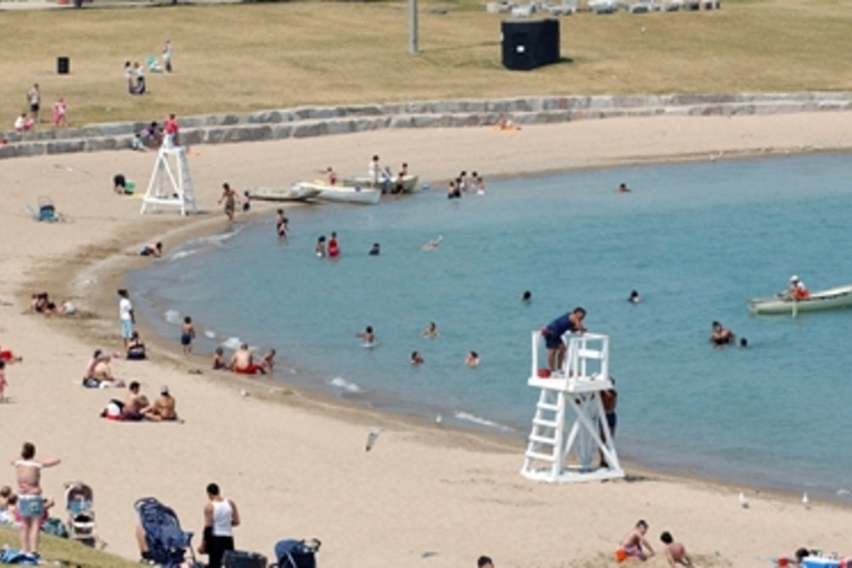 Crowded beach with people swimming and sunbathing. Lifeguard stands watch.