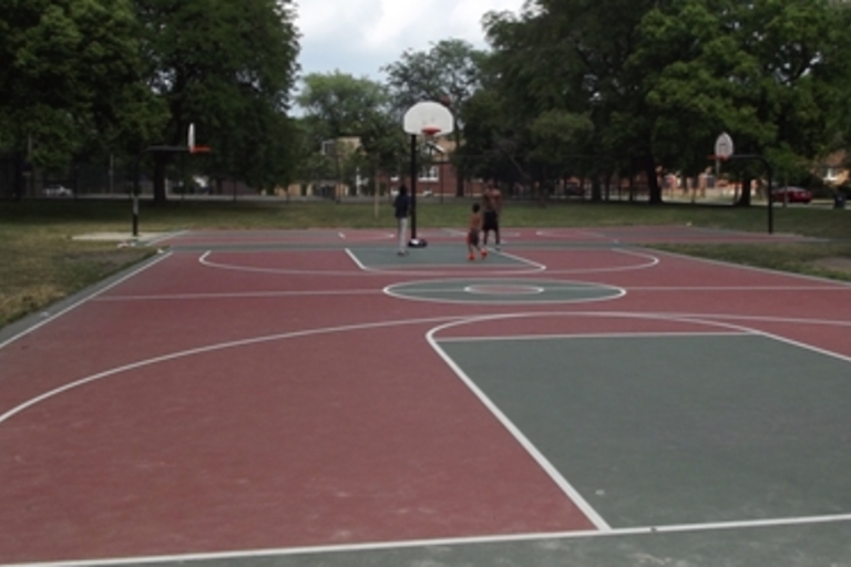 Outdoor basketball court with a few people playing.