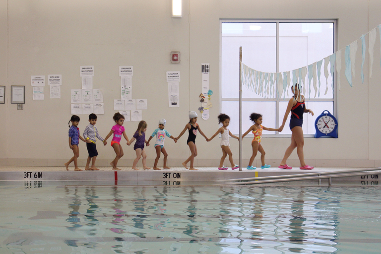 Children holding hands at edge of pool with instructor.