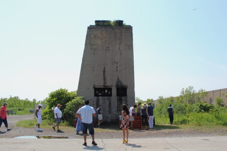 A tall, weathered concrete structure with small openings near the base.  People stand near it, some facing it, some walking away.
